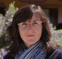 Kerry Scott pictured with glasses and a blue and white scarf in a garden setting.